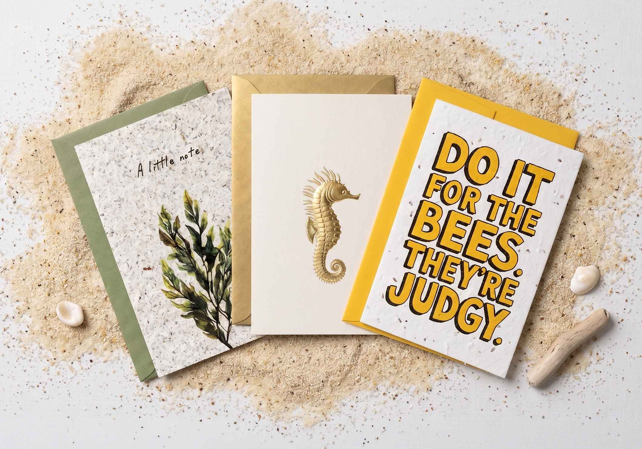 Three greeting cards from our plantable, foil-pressed and seaweed collections, arranged on Cornish sand.